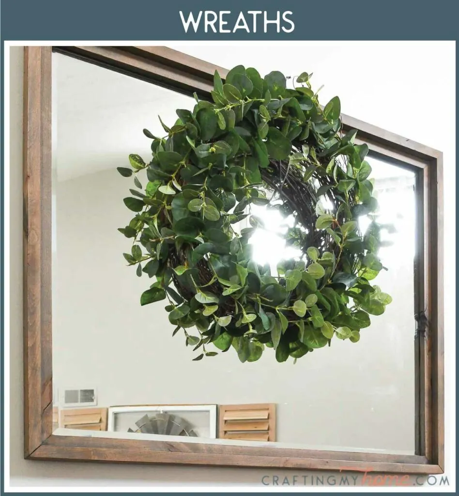 Picture of eucalyptus wreath hanging on a large mirror with a navy box around it and white text: Wreaths.
