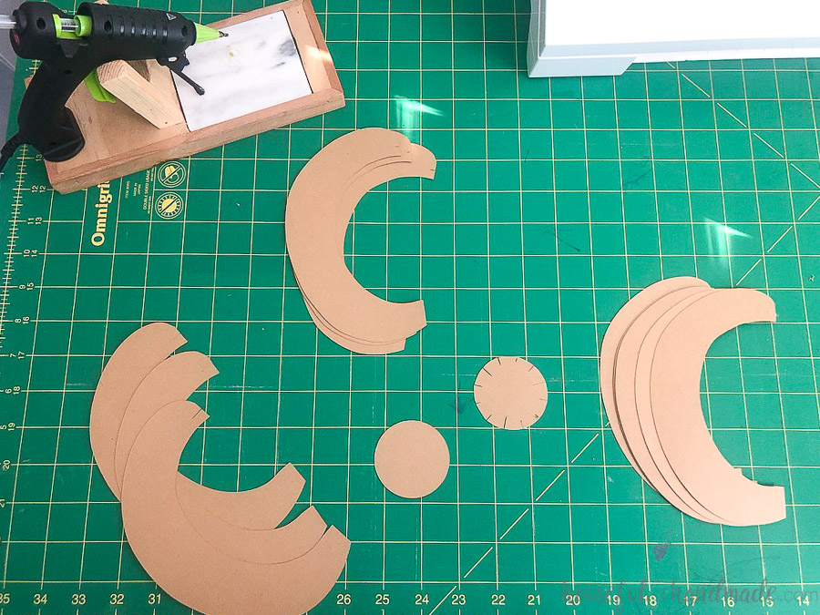 All the pieces of the 3d paper pumpkins cut out of brown craft paper laying on a green cutting mat.