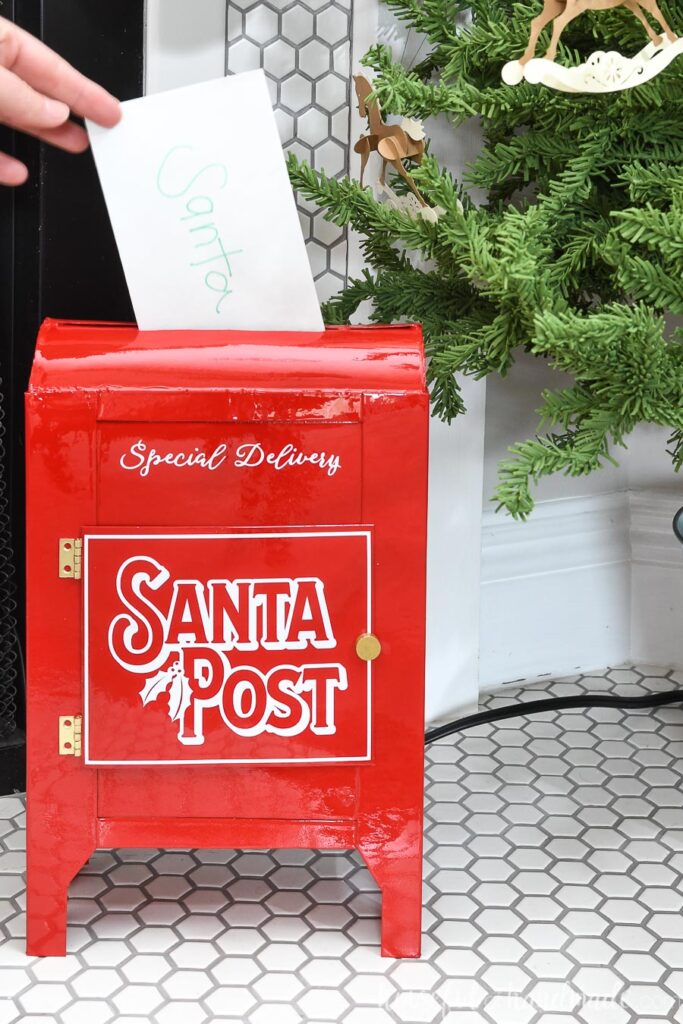 Shiny red Santa mailbox with letter being slid in the top.