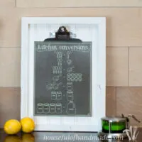 Chalkboard printable kitchen conversion chart on a clipboard with a salt cellar and lemons in front of it.