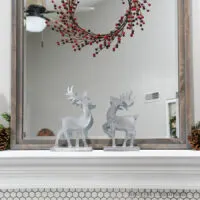 Two Christmas reindeer decorations on the mantel in front of the mirror with classic mantel decor.