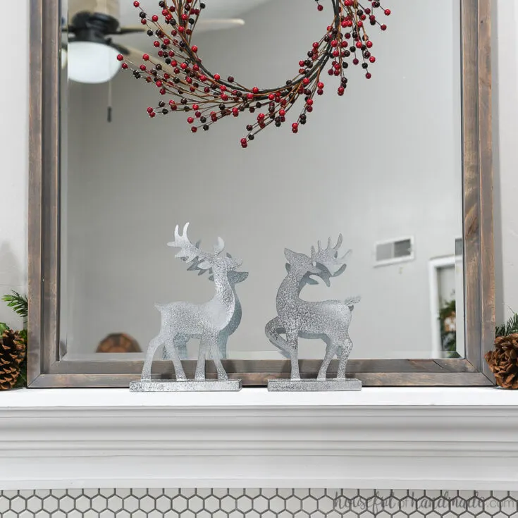 Two Christmas reindeer decorations on the mantel in front of the mirror with classic mantel decor.
