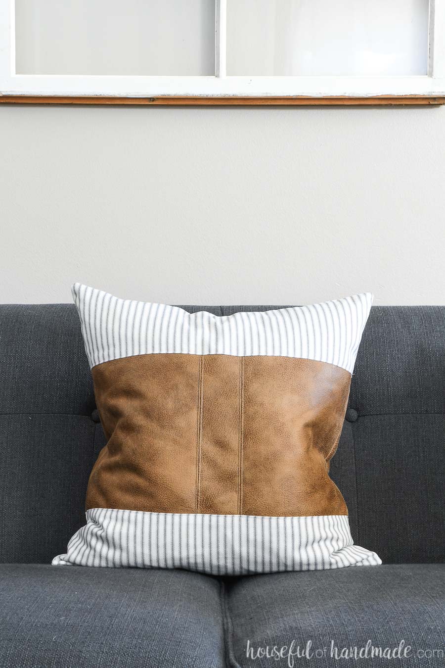 Leather pillow cover with center stripe and ticking fabric on a navy sofa.