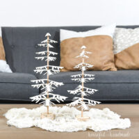 DIY paper Christmas trees made by placing branches on a dowel, sitting on a table.