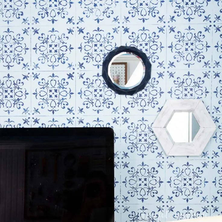 Two wall mirrors, one white hexagon and one blue geometric, hanging on a blue and navy stenciled wall.