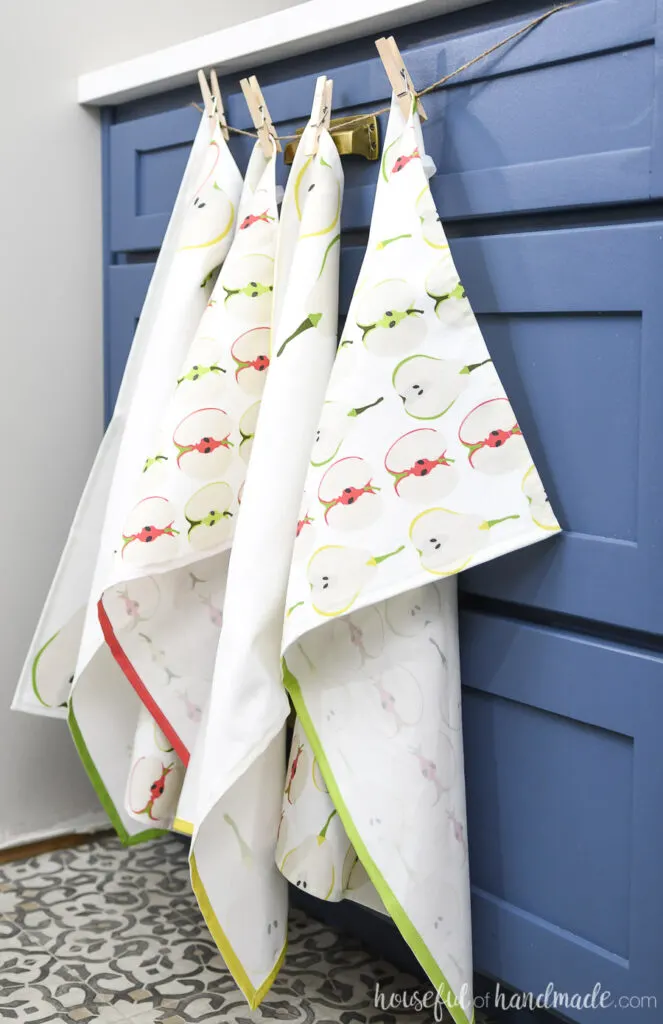 Four DIY tea towels hanging in front of a blue drawer cabinet. 