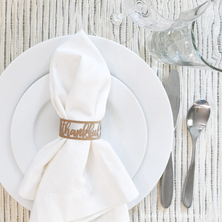 Paper Thanksgiving napkin ring around a white napkin on a place setting.
