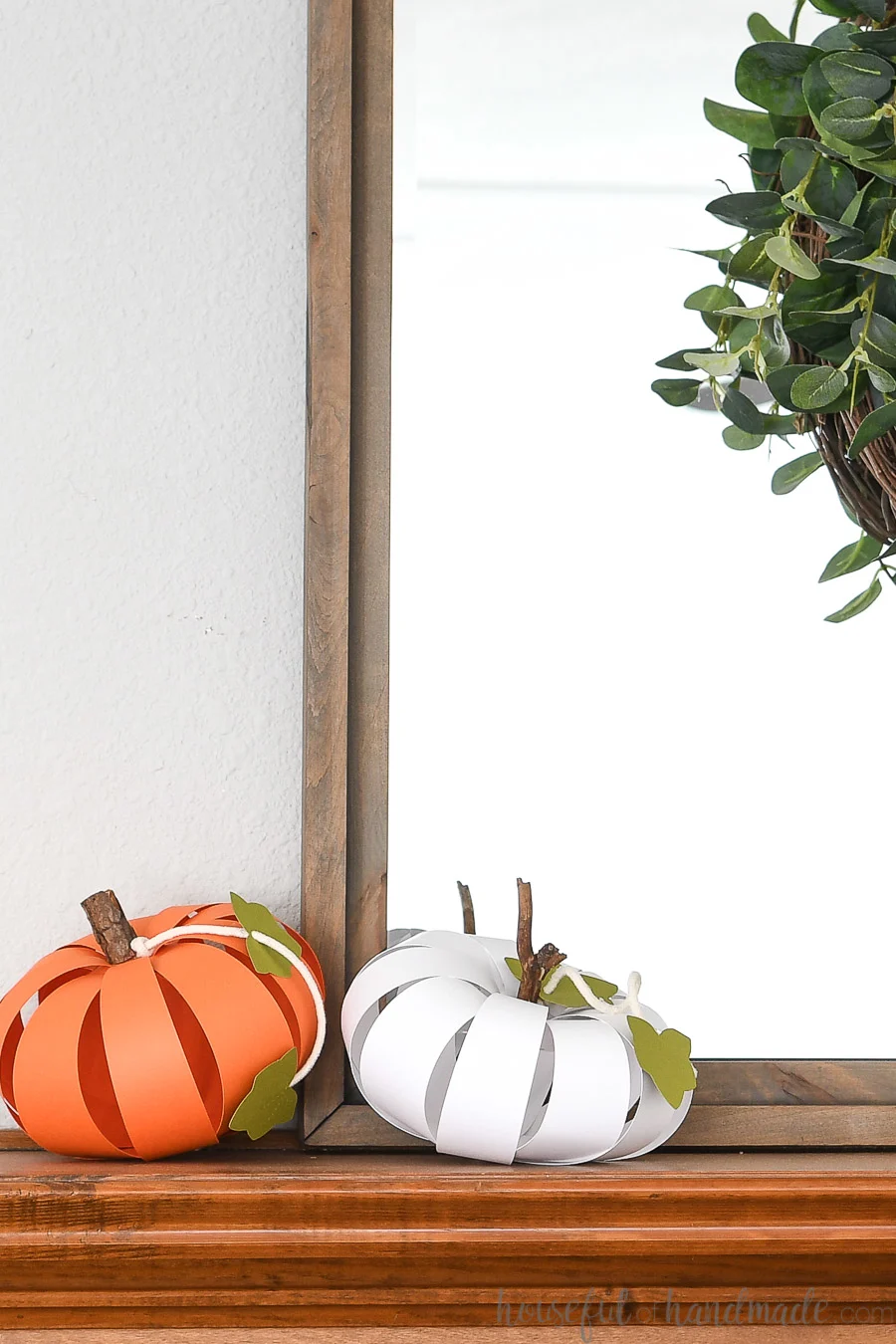 White and orange paper pumpkins on the mantel in front of a gray framed mirror.
