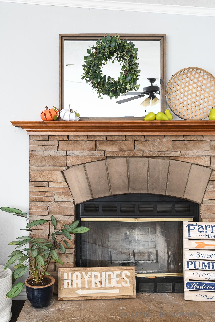 Stone fireplace with wood mantel decorated for fall with wood signs, a mirror, and paper pumpkins. 