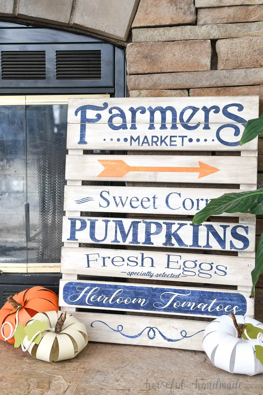 Farmers Market pallet sign on the fireplace hearth with 3 DIY paper pumpkins on the hearth in front of it.