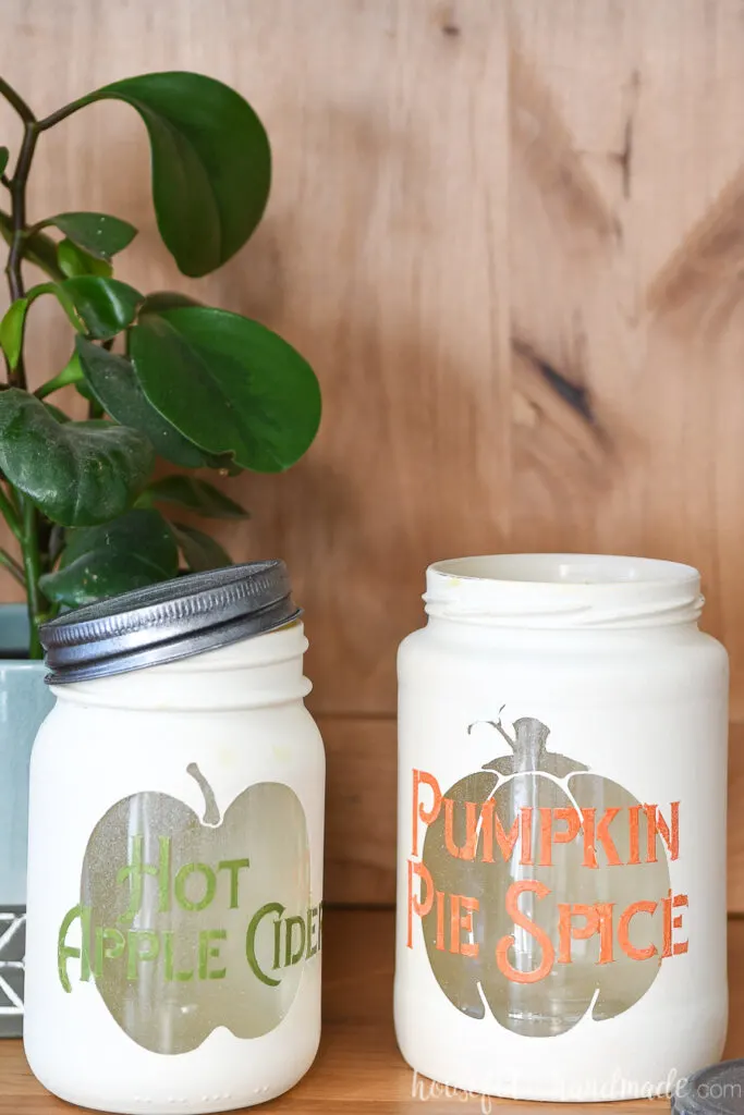 Close up of the two completed fall kitchen canisters, one with a pumpkin shape and the words pumpkin pie spice on it and the other with and apple shape and the words hot apple cider on it. 
