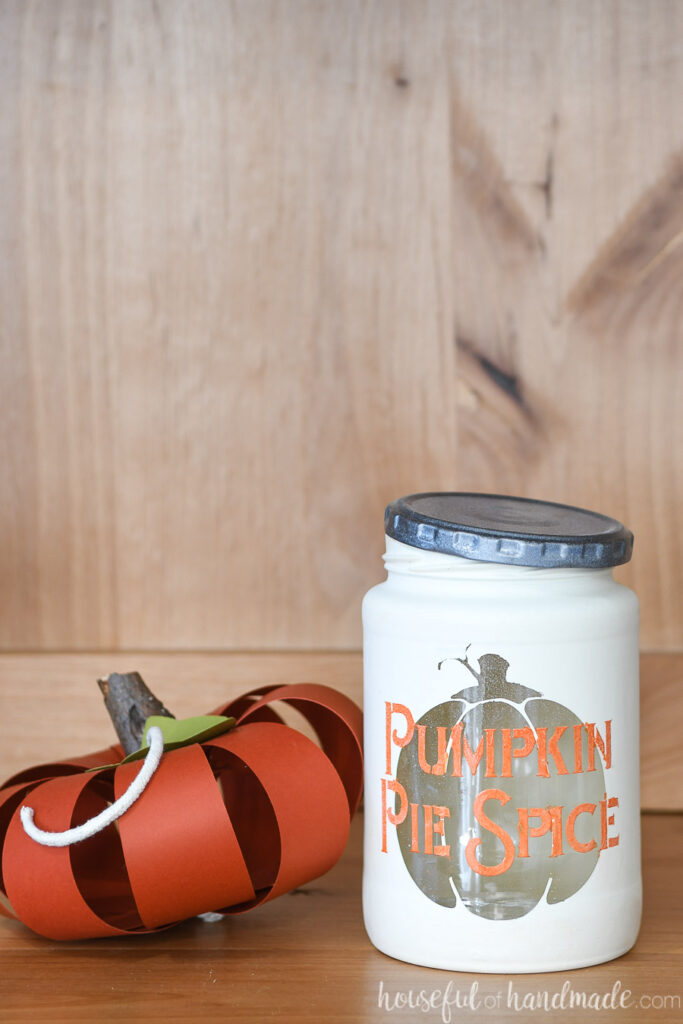 Close up of the Pumpkin Pie Spice kitchen canister next to a paper pumpkin craft. 