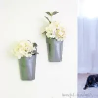 White wall with faux metal wall vases hanging on it, filled with white hydrangea flowers.