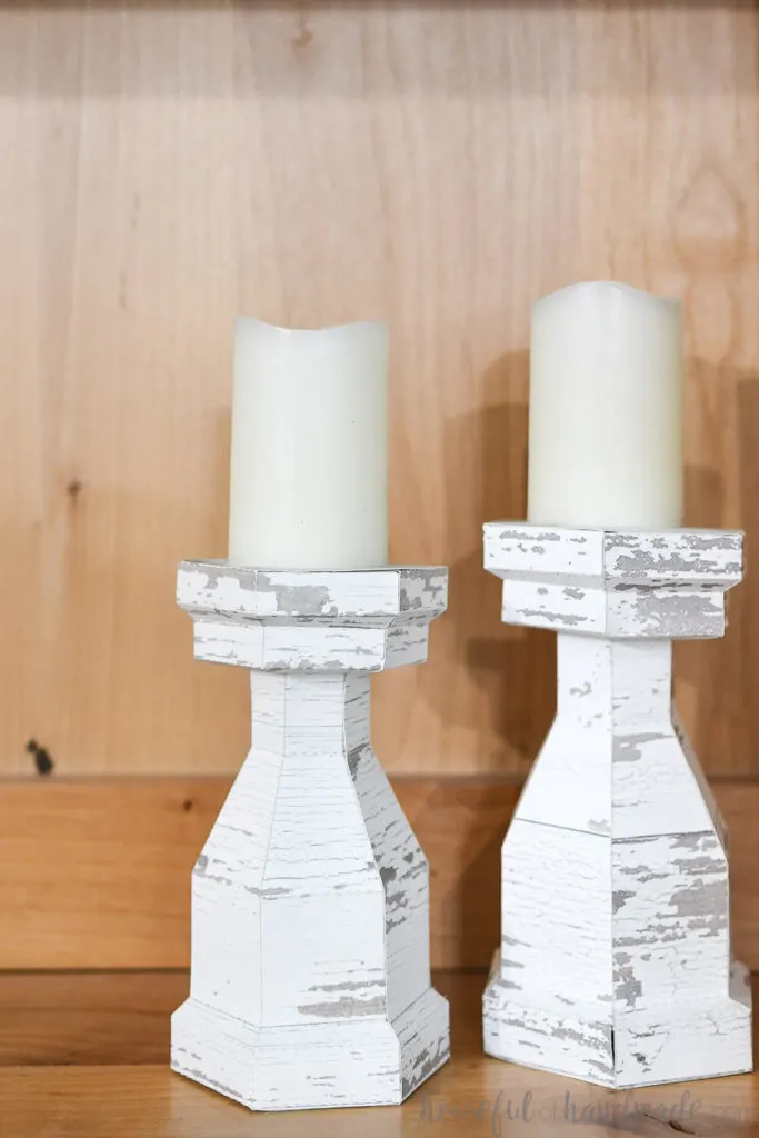 Two chunky candlesticks with chippy white paint texture in a bookcase. 