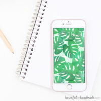 iPhone vertically placed on a white note book displaying a tropical leaf watercolor pattern.