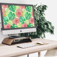 iMac on a desk with digital water color art of hibiscus. Plant in the back round and keyboard and mouse on the desk.