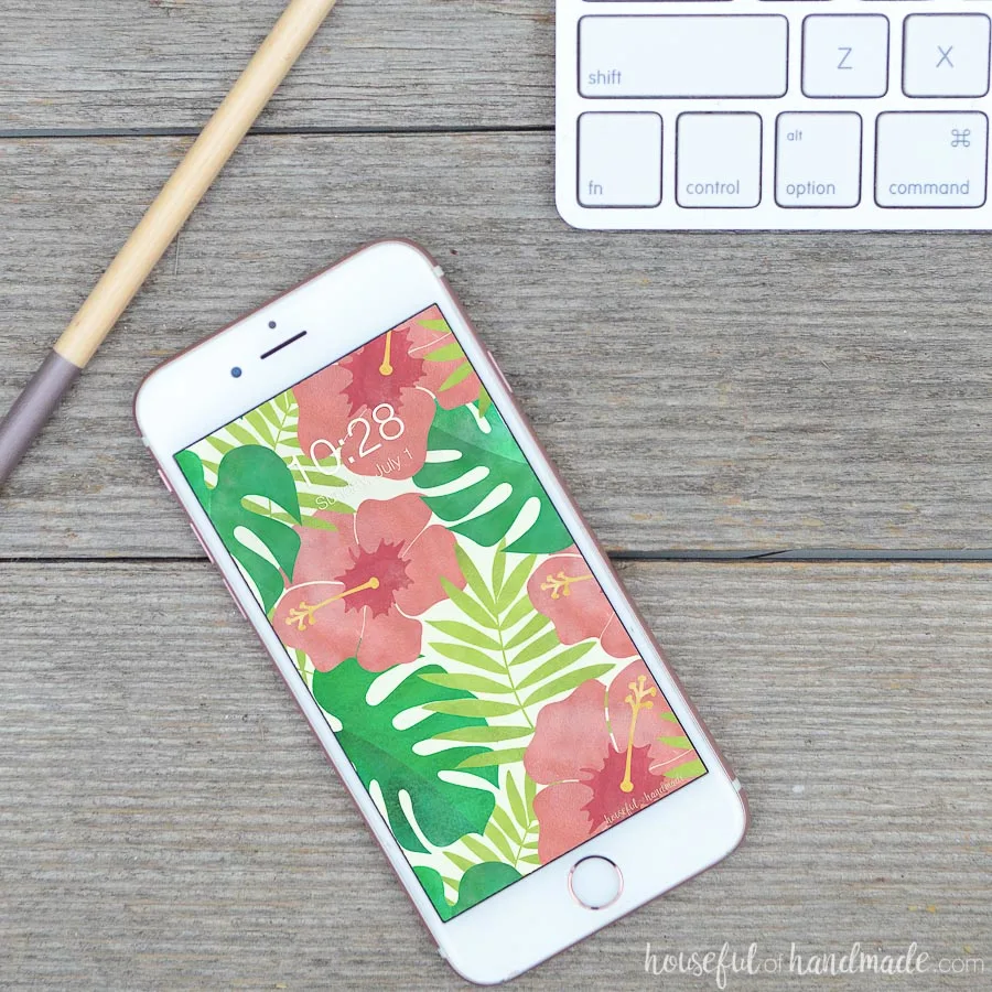 iPhone with hibiscus water color digital background on wooden desk with pencil and keyboard.