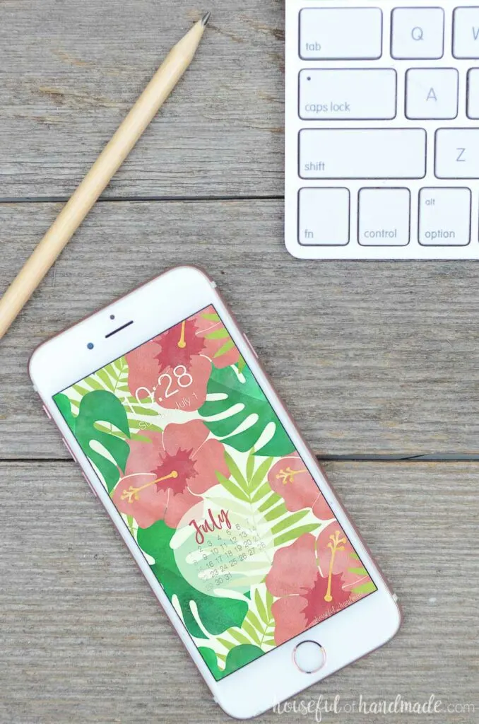 cell phone at an angle on a wood desk displaying watercolor digital background with a calendar.