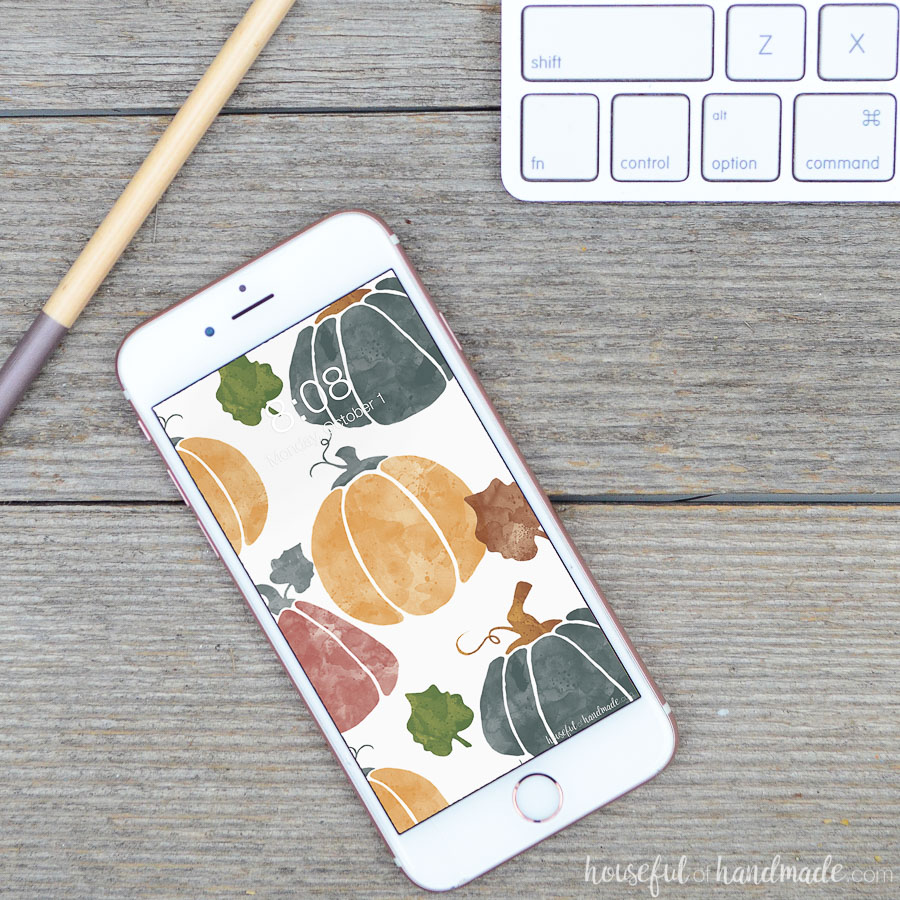 Watercolor pumpkin digital wallpaper on a white iPhone.