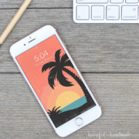 Rose gold iPhone with a retro tropical sunset digital wallpaper on the home screen.