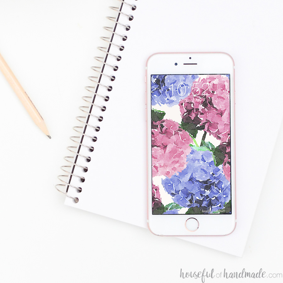 Notebook and pencil with smartphone on top of it with hydrangea free digital wallpaper design on it.