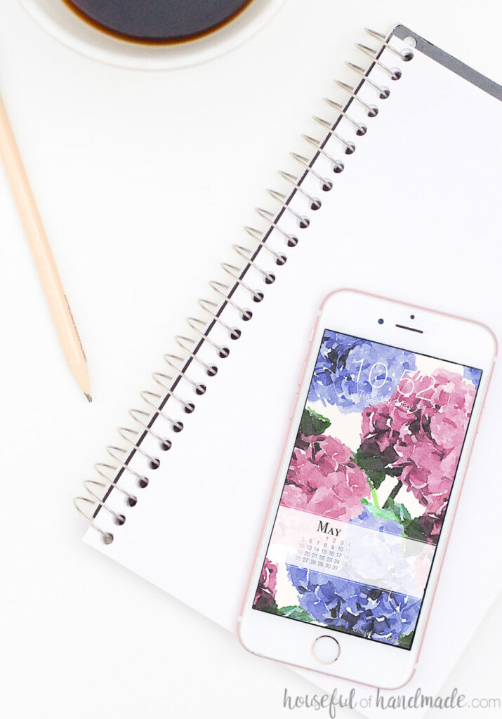 White iPhone with blue and pink hydrangea digital wallpaper design on the screen. 