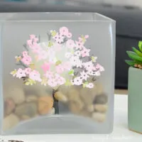 Large glass candle holder decorated with a frosted tree and spring blossoms on a tray in a living room.