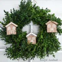 Three paper Christmas ornaments that look like gingerbread houses hanging in a wreath.