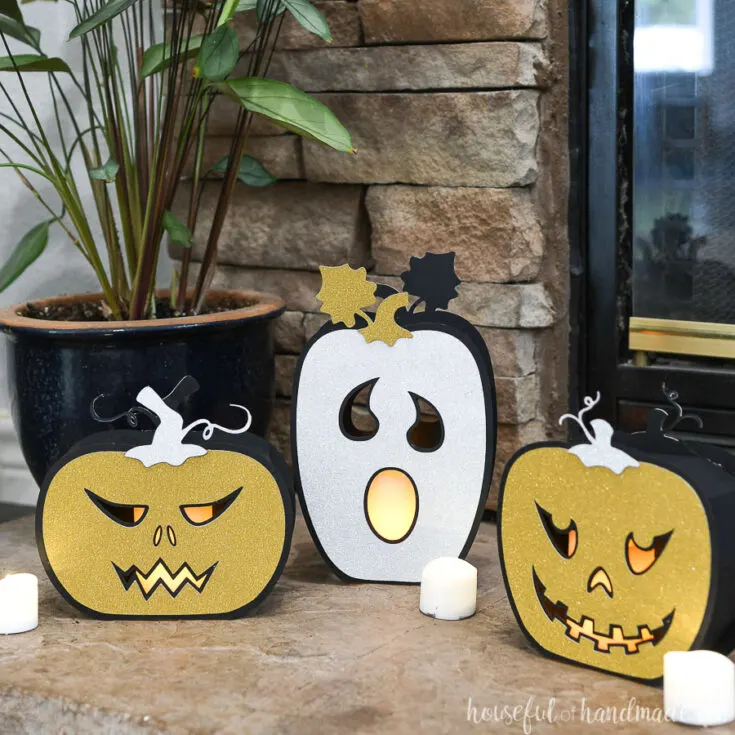 Three Halloween pumpkin lanterns made from black and glitter cardstock, sitting in front of a fireplace.