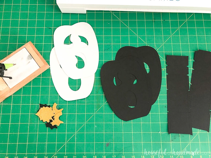 Ten pieces for the tall ghost face paper jack-o-lantern cut out of cardstock sitting on a green cutting mat.