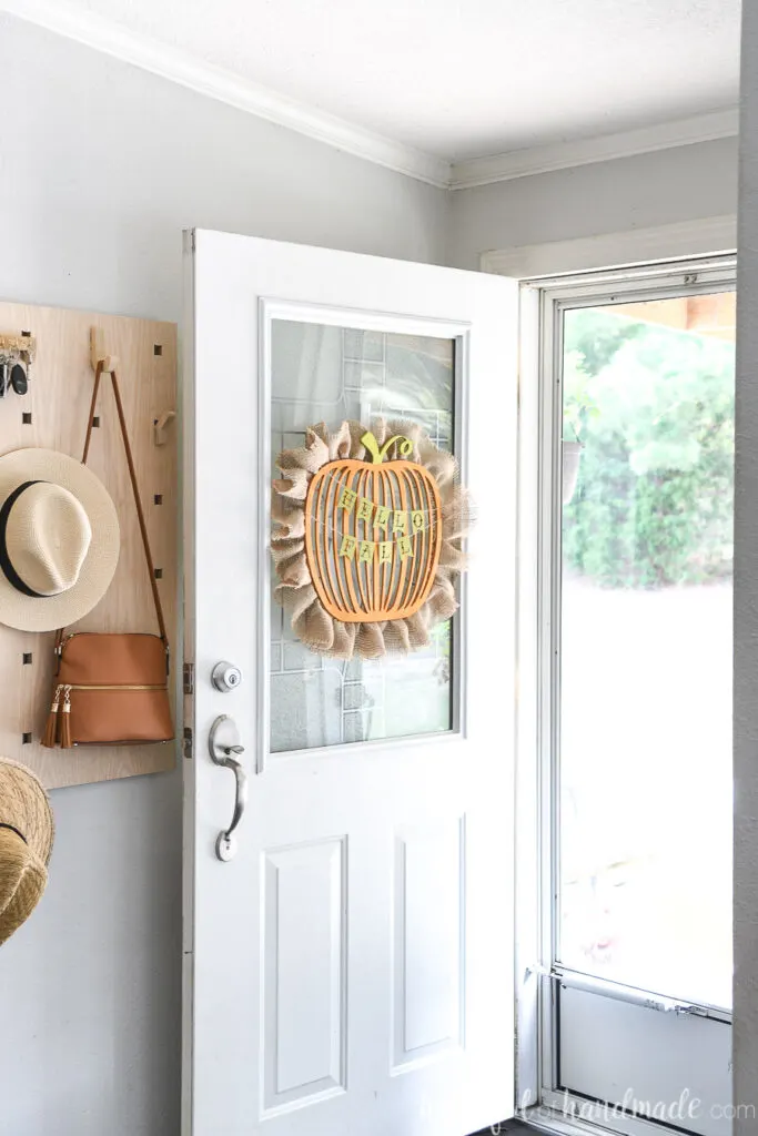  Entryway with door to the outside open and a wood pumpkin wreath hanging on it.