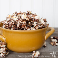 Yellow dish full of dark chocolate caramel popcorn with some spilling over the sides.