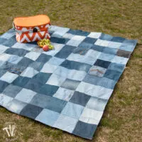 Picnic table made from recycled jeans sitting on the grass with an orange picnic basket on it.
