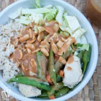 Bowl of brown rice with sautéed vegetables with peanut sauce on top.
