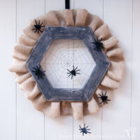 Halloween wreath made from wood hexagon with spiderweb woven in the center and burlap ribbon along the outside.