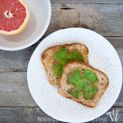 Two slices of wheat toast with green eggs in the shape of shamrocks cooked in the center.