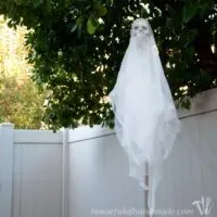Outdoor Halloween decoration of a skull ghost craft hanging in a tree.
