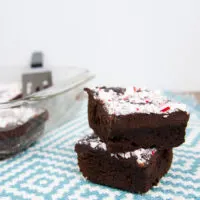 Two chewy chocolate brownies with peppermint ganache in a stack on a blue and white tablecloth.