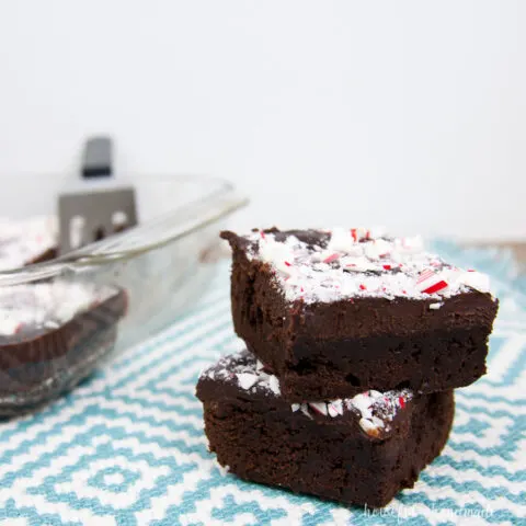 Two chewy chocolate brownies with peppermint ganache in a stack on a blue and white tablecloth.