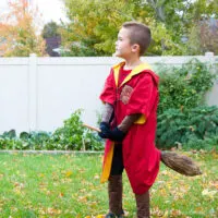 Young boy wearing a DIY Harry Potter Quidditch costume in red for the Gryffindor team and riding a DIY broom.