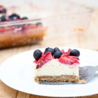 Oatmeal cheesecake berry bar on a plate with the pan of remaining bars in the background.