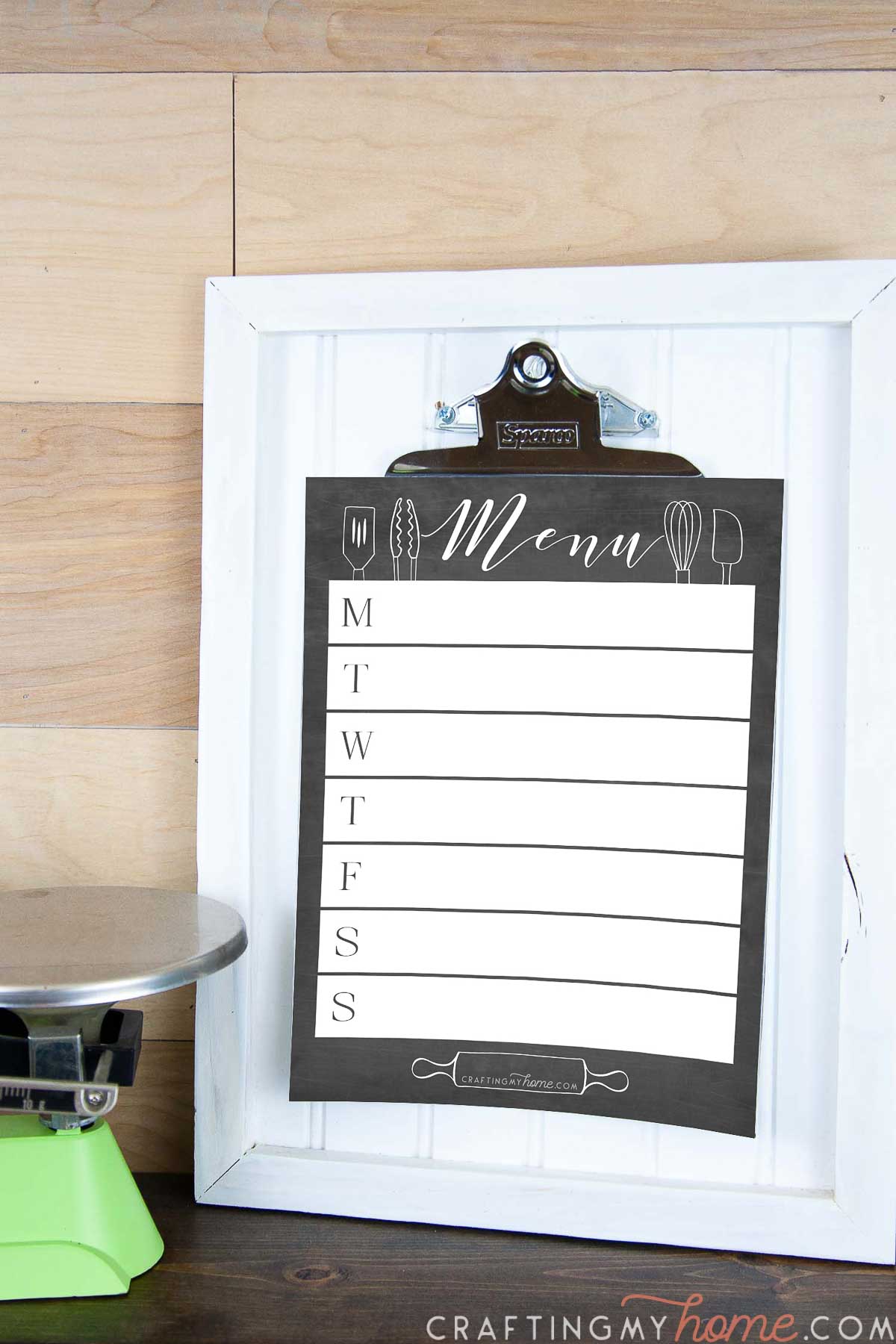 Close up of the white clipboard with a chalkboard design printable menu board on it next to a green scale. 
