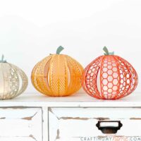 Cream, yellow-orange, and orange paper pumpkin lanterns in 3 different patterns and sizes sitting on a side table.