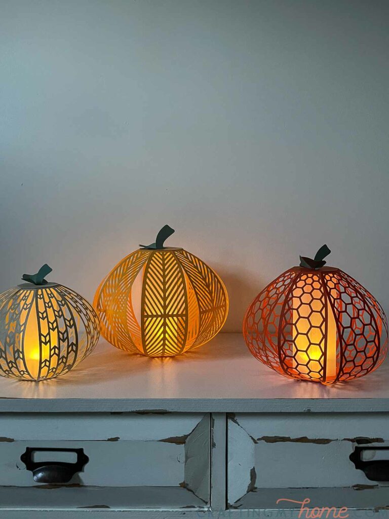 Three pumpkin lanterns made from paper with flameless tea lights in them glowing in the dark. 