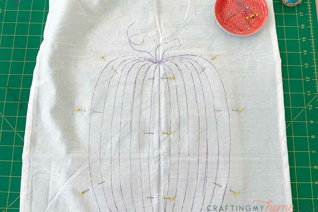 Fabric stabilizer pinned to the back of the tea towel with pumpkin design drawn on it. 