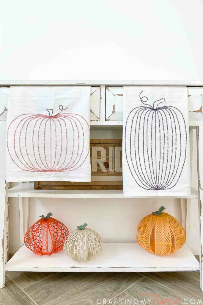 Homemade tea towels with pumpkin designs on them hanging from the draws of a white chippy console table. 