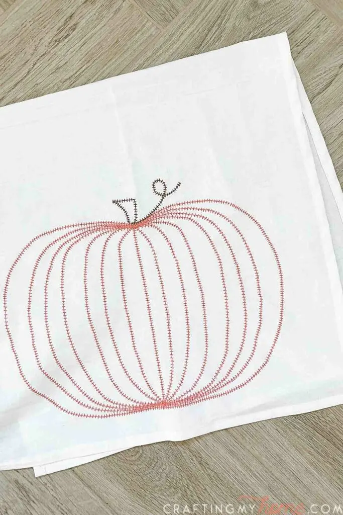 Coral colored DIY embroidered pumpkin on a white tea towel.