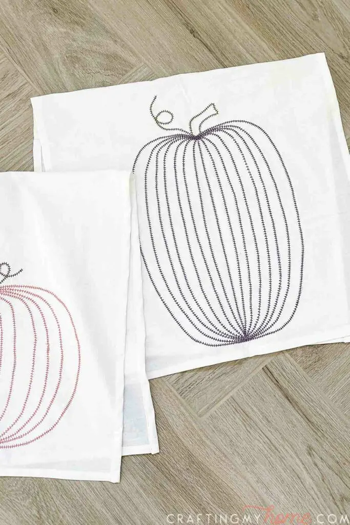 DIY pumpkin tea towels with two different shaped pumpkin designs sewn on them laying on a wood background. 