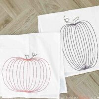 Two DIY pumpkin tea towels with a simple pumpkin design sewn into the fabric laying on a wood background.