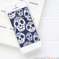 White iPhone with blue and white sugar skull pattern as the digital wallpaper on the home screen.